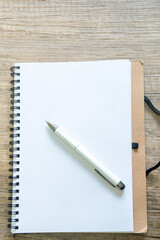 A paper notebook open to a blank page on an oak desk with a pen. Concept: start written list of...