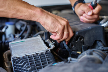 Close-up view of mechanic using ratchet tool to repair car engine under open hood. Auto service,...
