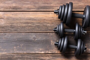 Three black adjustable dumbbells on a rustic wooden surface