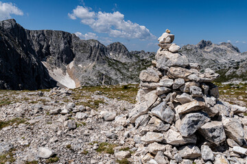 Stone cairn on a rocky alpine plateau with dramatic mountain peaks and patches of snow. Clear blue...