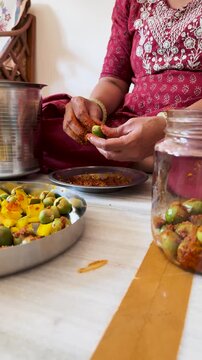 4K Vertical video of Indian woman wearing bangles in hand pouring pickle in glass jar. Homemade mango and glue berry pickle. Preservation of food. Indian home maker female making fresh food at home
