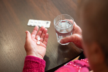 Senior woman holding pills and glass of water. Elderly woman with two tablets and glass of water in...