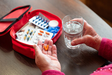 Elderly woman taking medicine from red first aid kit box. Senior woman taking capsules and holding...
