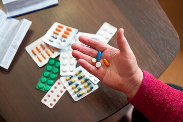 Senior woman's hand with blue capsule. Elderly woman holding blue capsule over a table with...
