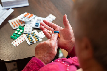 Elderly woman examining pills in hand. Senior woman looking at capsules and tablets in hand before...