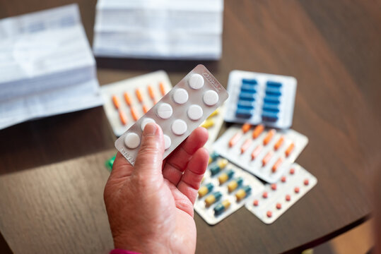 Senior woman choosing white pills from table. Elderly woman selecting white pills among other medications and leaflets, reflecting daily healthcare management