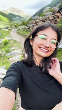 4K Vertical selfie shot of Indian girl enjoying summer holidays in mountains in Sural Bhatori, Himachal Pradesh, India. Travel, tourism and hiking outdoors concept. Girl having fun while trekking. 