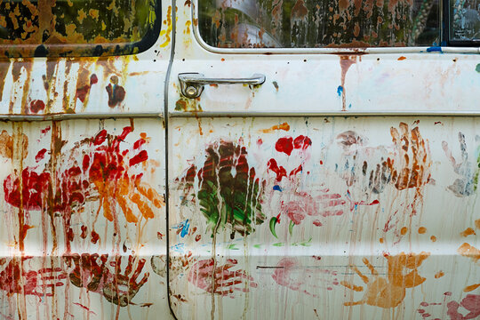 An old white car covered in colorful handprints and paint streaks.