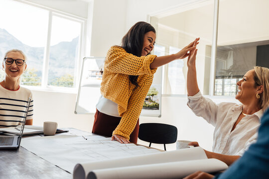 Team collaborating in small architecture firm celebrating success with high five