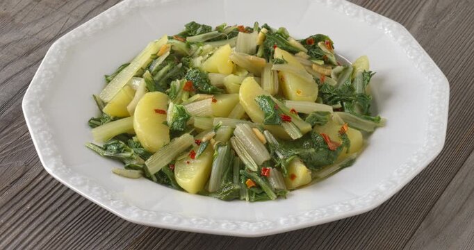 South Croatian Blitva s Krumpirom dish on a white plate. The dish is made with boiled potatoes, swiss chard, garlic, and olive oil. Table spin.