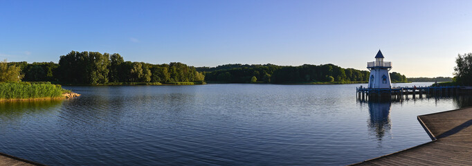 Panoramic photo of Lake L'Ailette (Laon, France) just before sunset, creating a beautiful clear blue sky. With forests and a small lighthouse.