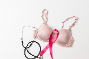 Pink bra, pink ribbon symbolizing breast cancer awareness, and a stethoscope on white background. Concept of women's health, breast cancer prevention, medical support, and awareness campaigns.