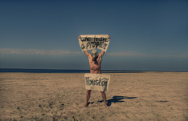 
Naked man in gas mask standing on a deserted beach, holding signs.