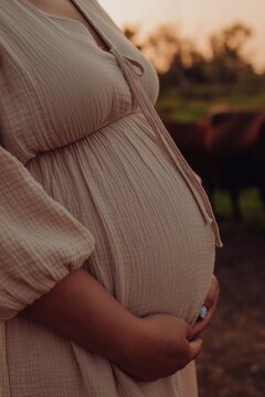 Beautiful pregnant belly close-up. Third trimester, pregnant woman hugs belly at sunset waiting for baby. Natural breathable muslin fabric, summer childbirth, walk, health of expectant mother and baby