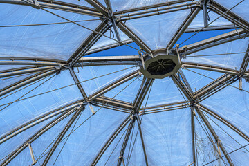 Obraz premium A close-up view of a modern transparent dome roof structure made of steel beams and plastic panels under a clear blue sky.