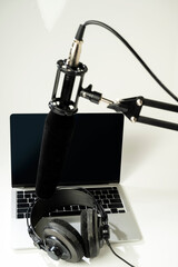 Studio microphone for podcasting or streaming on a boom arm with a laptop and headphones on a white background. Mockup or Copy space