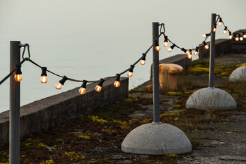 An outdoor garland of beautiful retro light bulbs on poles with concrete bases creates a cozy...
