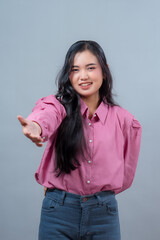 Portrait of a young Indonesian woman smiling and extending her arm forward as if offering help or...
