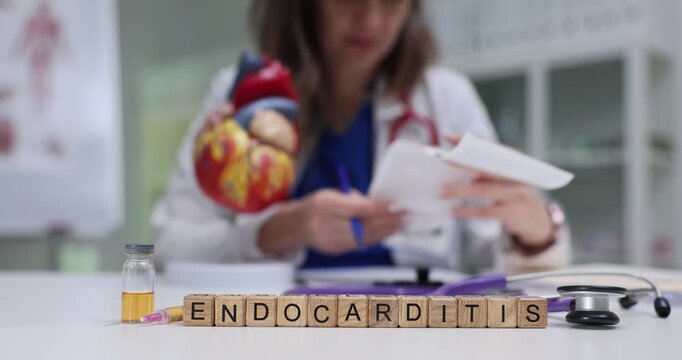 Word Endocarditis appears on wooden blocks positioned near heart model. Medical scan and liquid-filled tube relate to cardiac infection analysis