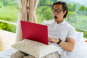 Surprised man working remotely with a laptop in a scenic nature resort - blending productivity with relaxation in the digital nomad lifestyle.