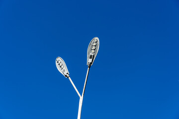 Two modern streetlamps tower upward under a bright blue sky, illuminating the city with their sleek...