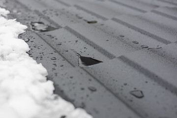 Water droplets gather on a textured metal surface alongside patches of melting snow, reflecting winter's chilly scene