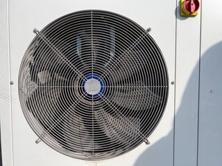 A large fan spins rapidly on an air conditioning unit, providing cool air during warm weather,...