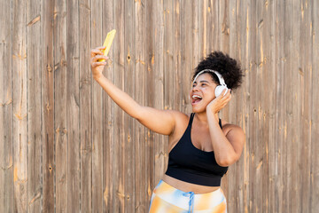 Happy curvy sportswoman taking selfie while listening music with headphones after workout outdoors