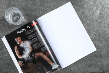 Open magazine and glass of water on grey background, top view. Mockup for design