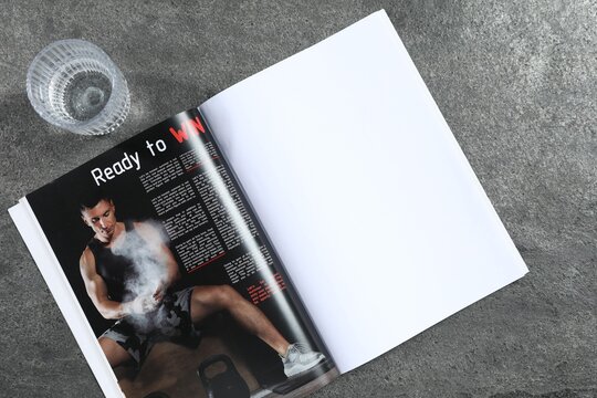 Open magazine and glass of water on grey background, top view. Mockup for design