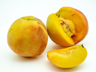 Ripe peaches, one sliced open, showcasing vibrant yellow flesh against a white background.
