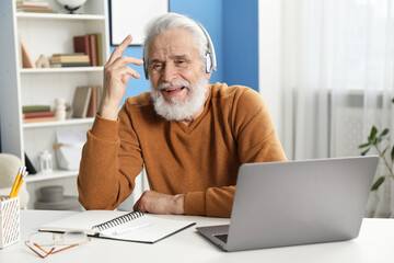 Senior man learning online using laptop at desk indoors. Self-study