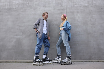Happy couple with roller skates near gray wall outdoors, low angle view