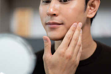 Skincare Routine. Young man applying moisturizer in front of mirror.