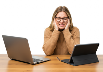 A stressed woman with her hands on her head, sitting at a desk with a laptop and tablet, looking frustrated isolated on transparent background