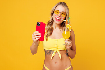 Young smiling woman wears bikini swimsuit rest near hotel pool drink citrus cocktail hold use...