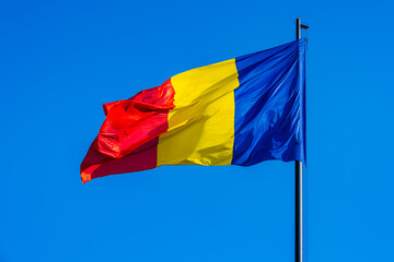 National flag of Romania flying in the wind; red yellow and blue flag on clear blue sky background