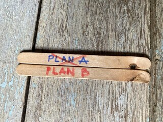 PLAN A' is crossed off in red ink on a wooden stick, with 'PLAN B' ready as the alternative.