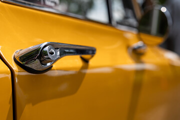 Close-up of a chrome door handle of a yellow classic car
