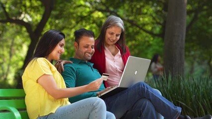 Indian man and woman using laptop and bank card at park.