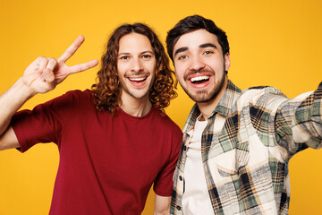 Close up young happy fun two friends buddies men they wear casual clothes together doing selfie shot pov on mobile cell phone show v-sign isolated on plain yellow orange background. Lifestyle concept.