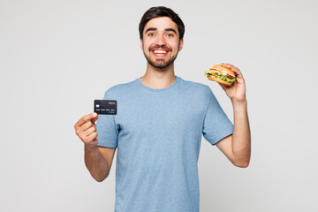 Young smiling fun man he wear blue t-shirt casual clothes hold mock up of credit bank card eat...