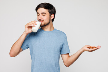 Young Caucasian man he wears blue casual clothes drink almond milk hold nuts in palm isolated on...