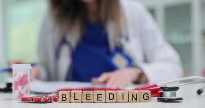 Word Bleeding made of wooden cubes put beside blood sample and red capsules. Dark red shades and tools reflect medical response to hemorrhage