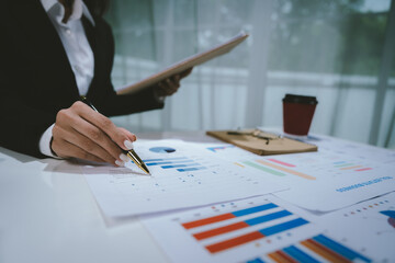 A professional businesswoman calculates financial data using a calculator, surrounded by charts and...