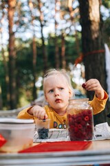 Little girl eating wild berries on camping table in forest