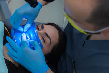 Dental treatment in progress: Female patient receiving care while the dentist applies a blue...