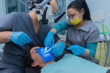 Dental Procedure Scene: Two Dental Professionals Perform a Treatment on a Patient Undergoing Oral Examination and Care with Specialized Equipment and Sterile Techniques