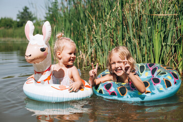 Happy children swimming with inflatable rings in lake during summer vacation