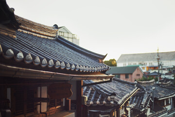 Naklejka premium Traditional Korean hanok rooftops in historic village with soft daylight and modern buildings in background